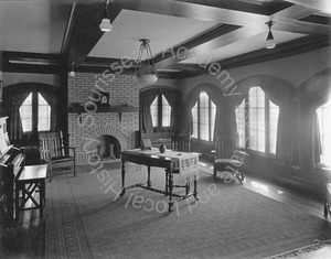 Image of View of living room with piano and table in center and fireplace at the far end