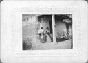 Image of Two unidentified women leaning against the front of an adobe structure